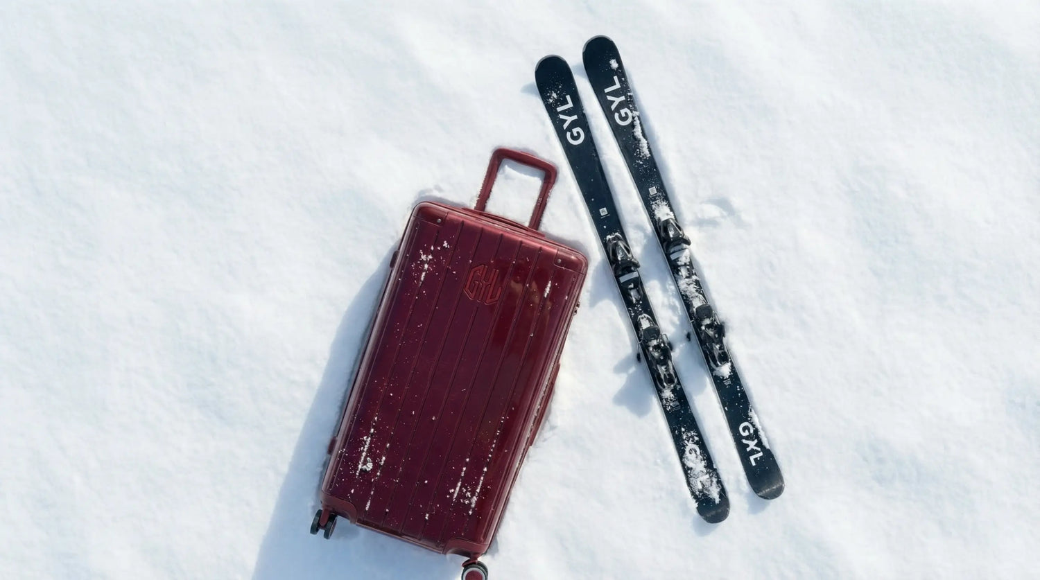 Valise rigide posée sur la neige à côté de skis, illustrant la préparation et le choix de l’équipement pour un séjour en station de ski