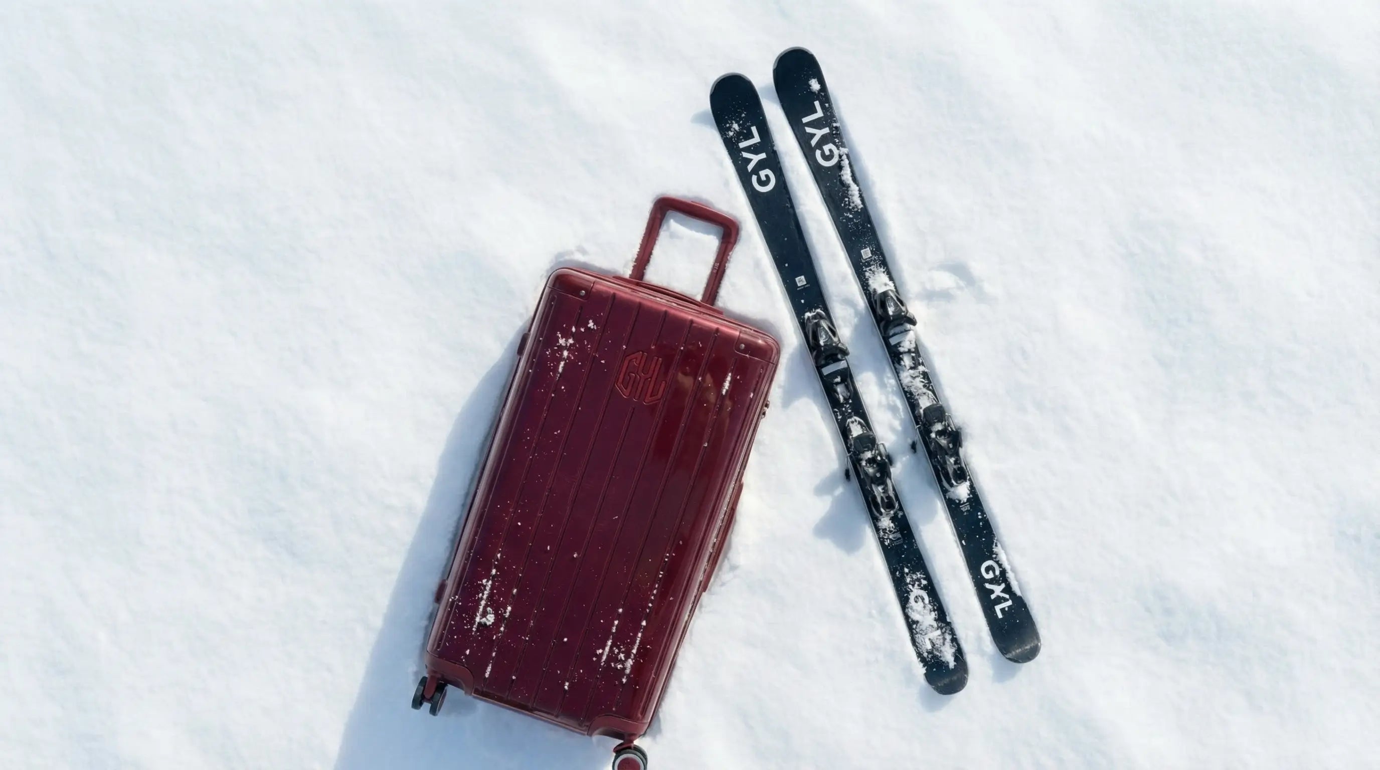 Valise rigide posée sur la neige à côté de skis, illustrant la préparation et le choix de l’équipement pour un séjour en station de ski