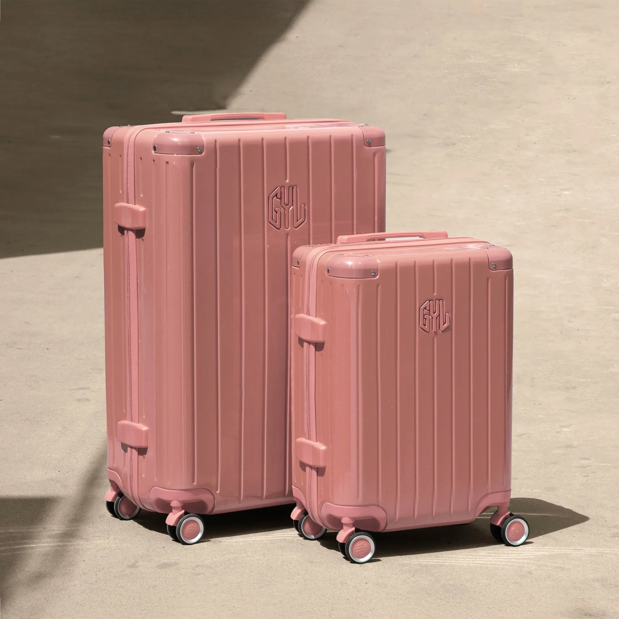 Ensemble de deux valises rigides GYL Intemporelle rose gold, tailles cabine et soute, posées sur sol béton.