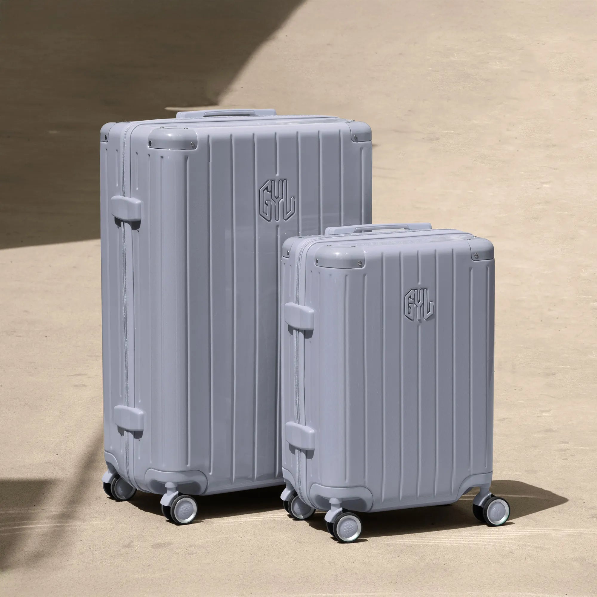 Ensemble de deux valises rigides GYL Intemporelle argent, tailles cabine et soute, posées sur sol béton.
