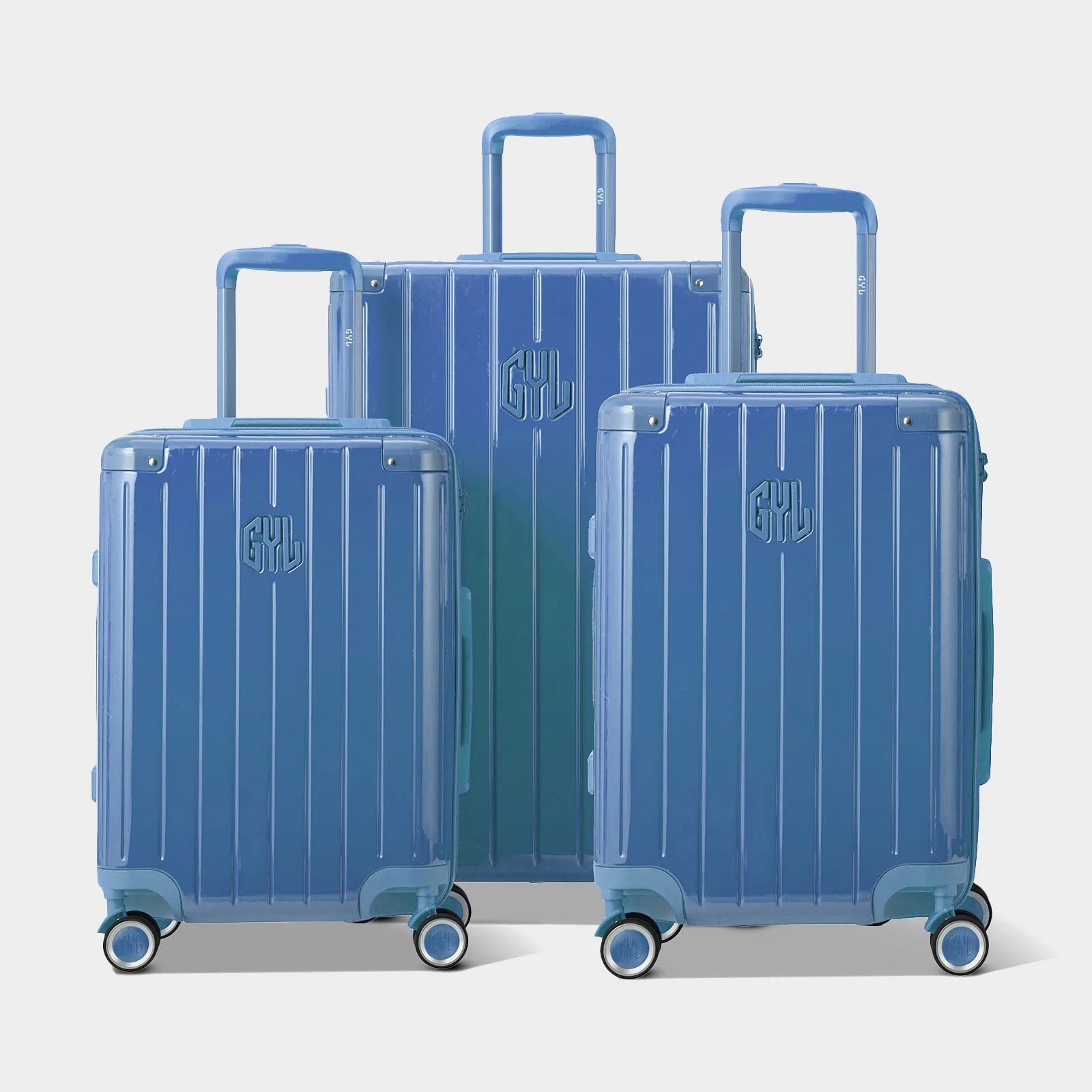 Trois valises rigides GYL Intemporelle bleu grisé, format cabine et soute, avec poignée trolley déployée.