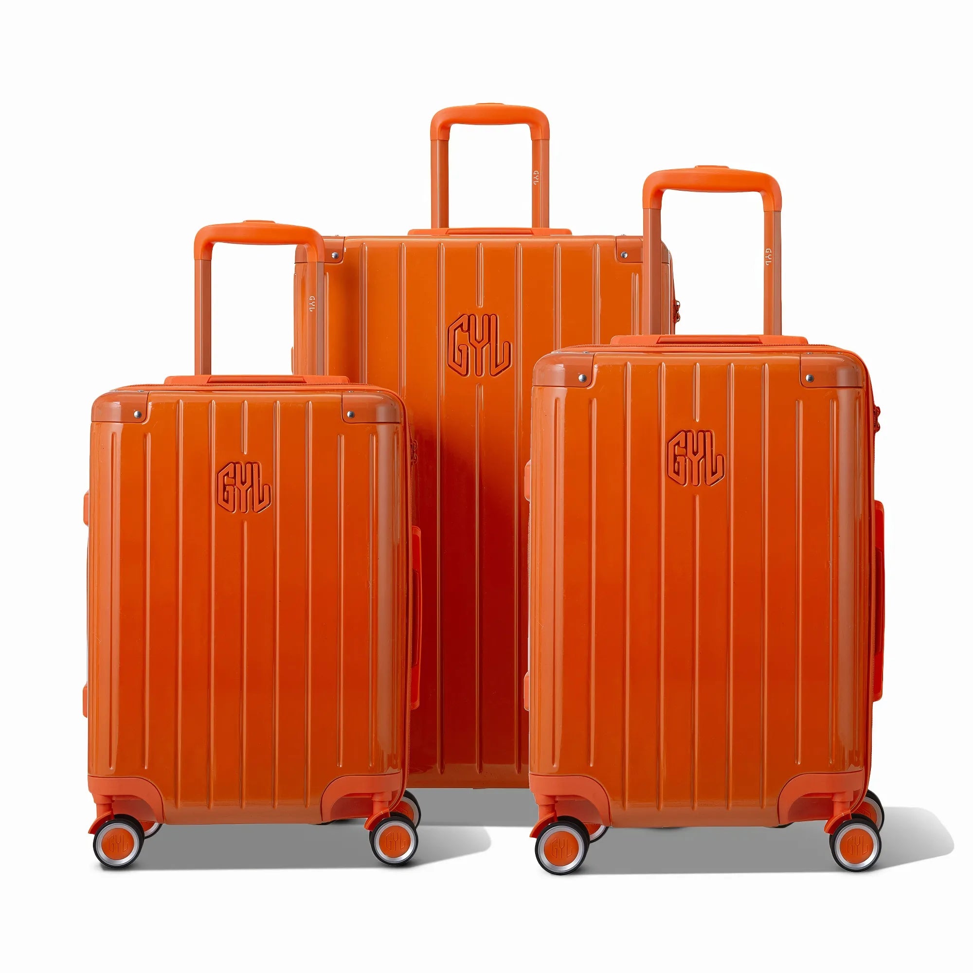 Trois valises rigides GYL Intemporelle orange, format cabine et soute, avec poignée trolley déployée.