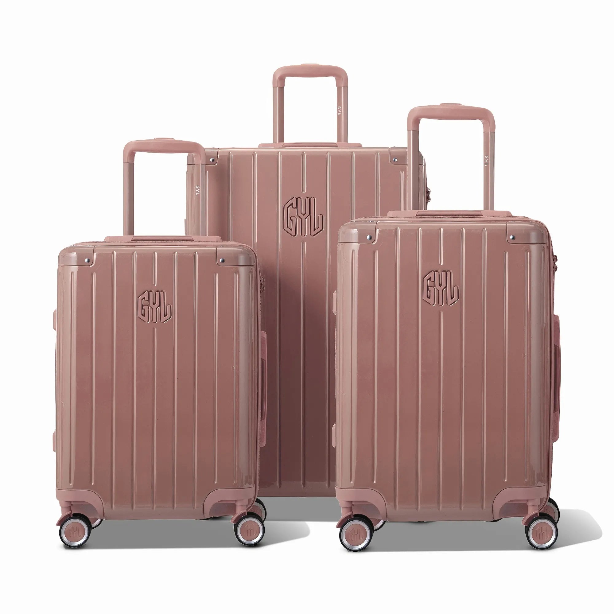 Trois valises rigides GYL Intemporelle rose gold, format cabine et soute, avec poignée trolley déployée.