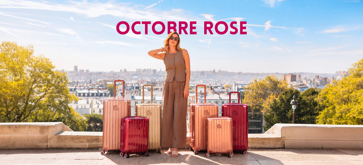 Octobre Rose chez GYL : femme posant sur une terrasse face aux toits de Paris, entourée de valises rigides GYL rose gold, champagne et rouge foncé