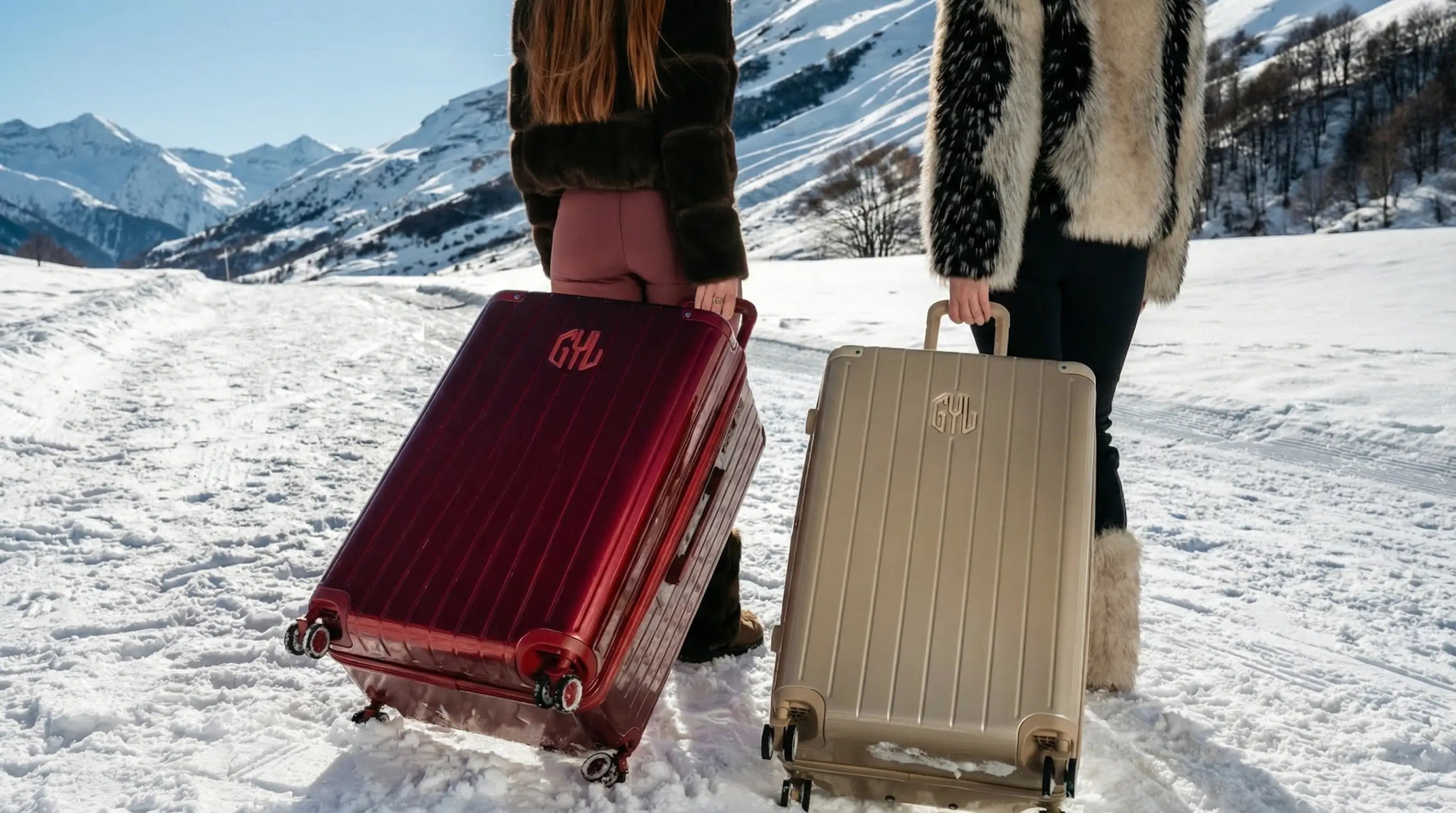 Deux valises rigides GYL rouge bordeaux et beige tirées sur la neige en montagne, scène de voyage hivernal avec paysage alpin enneigé