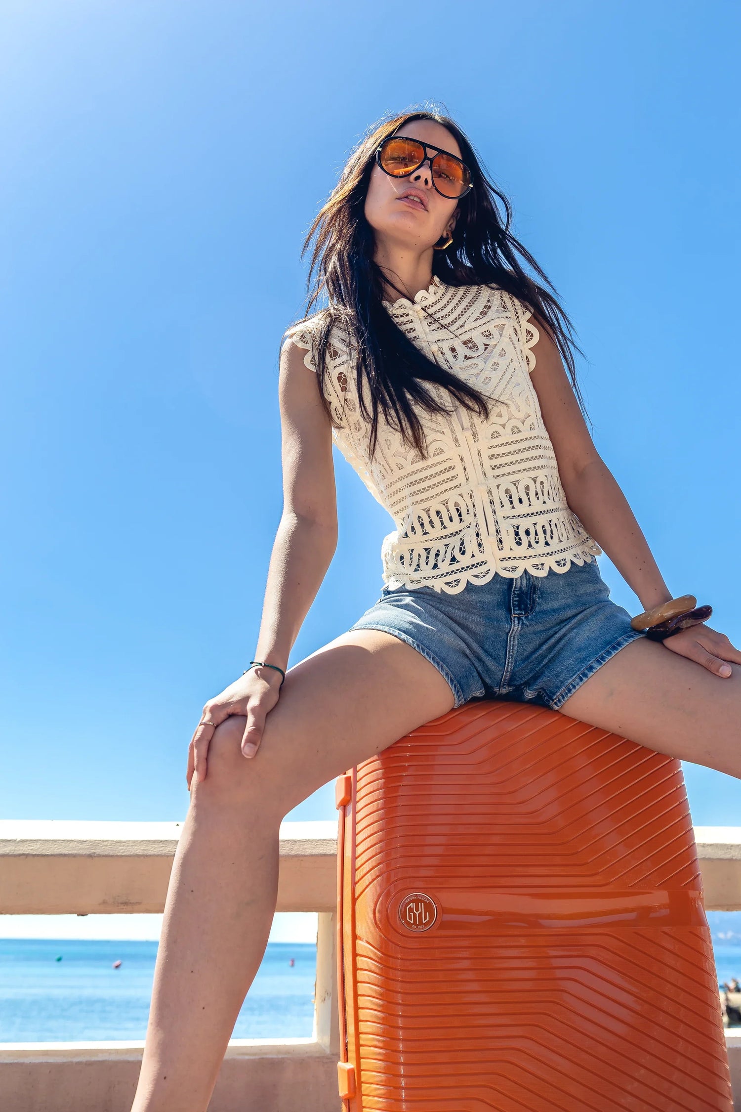 Valise cabine Signature coloris sapin tenue par une femme en robe en jean devant un palace illumine au crepuscule, lifestyle GYL