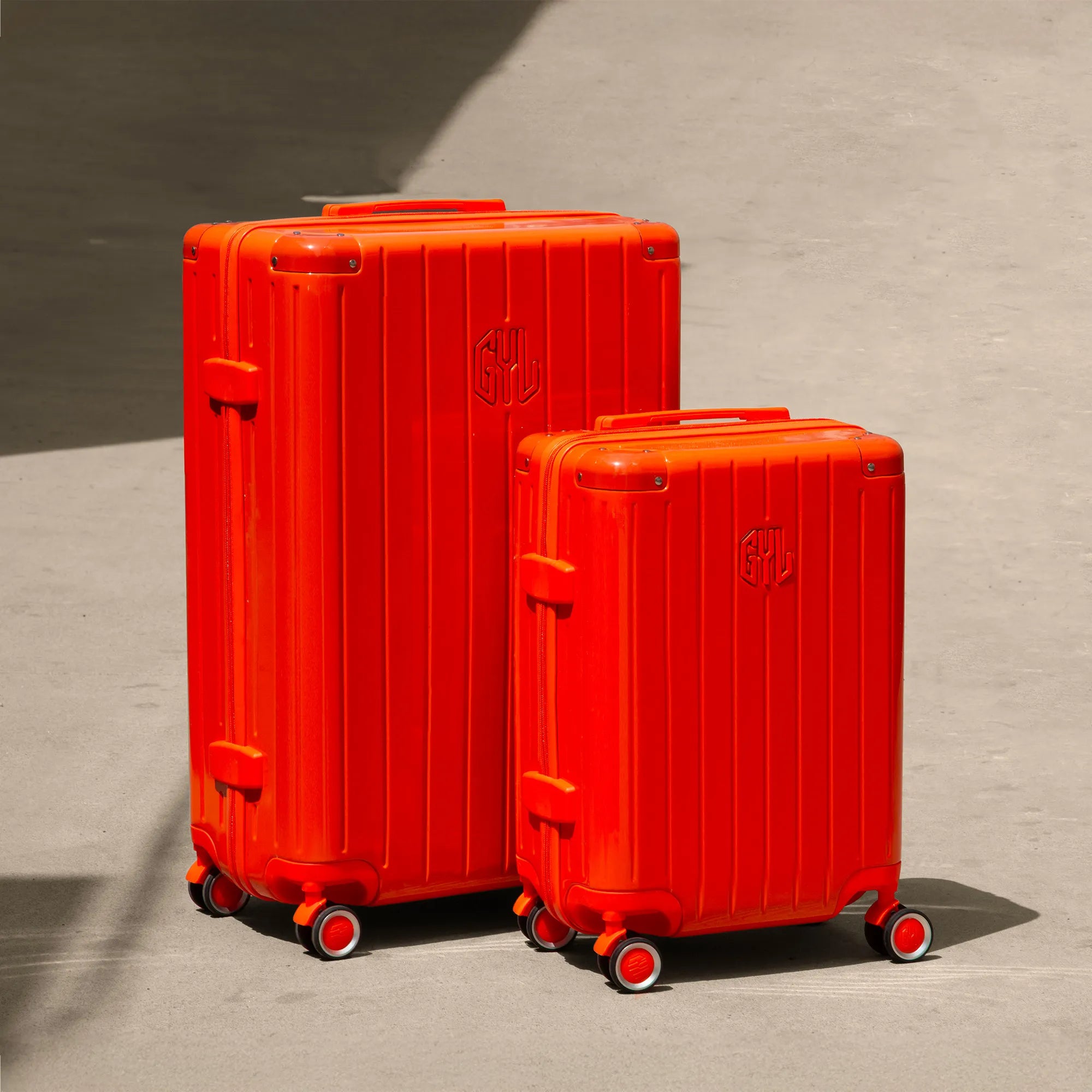 Ensemble de deux valises rigides GYL Intemporelle orange, tailles cabine et soute, posées sur sol béton.