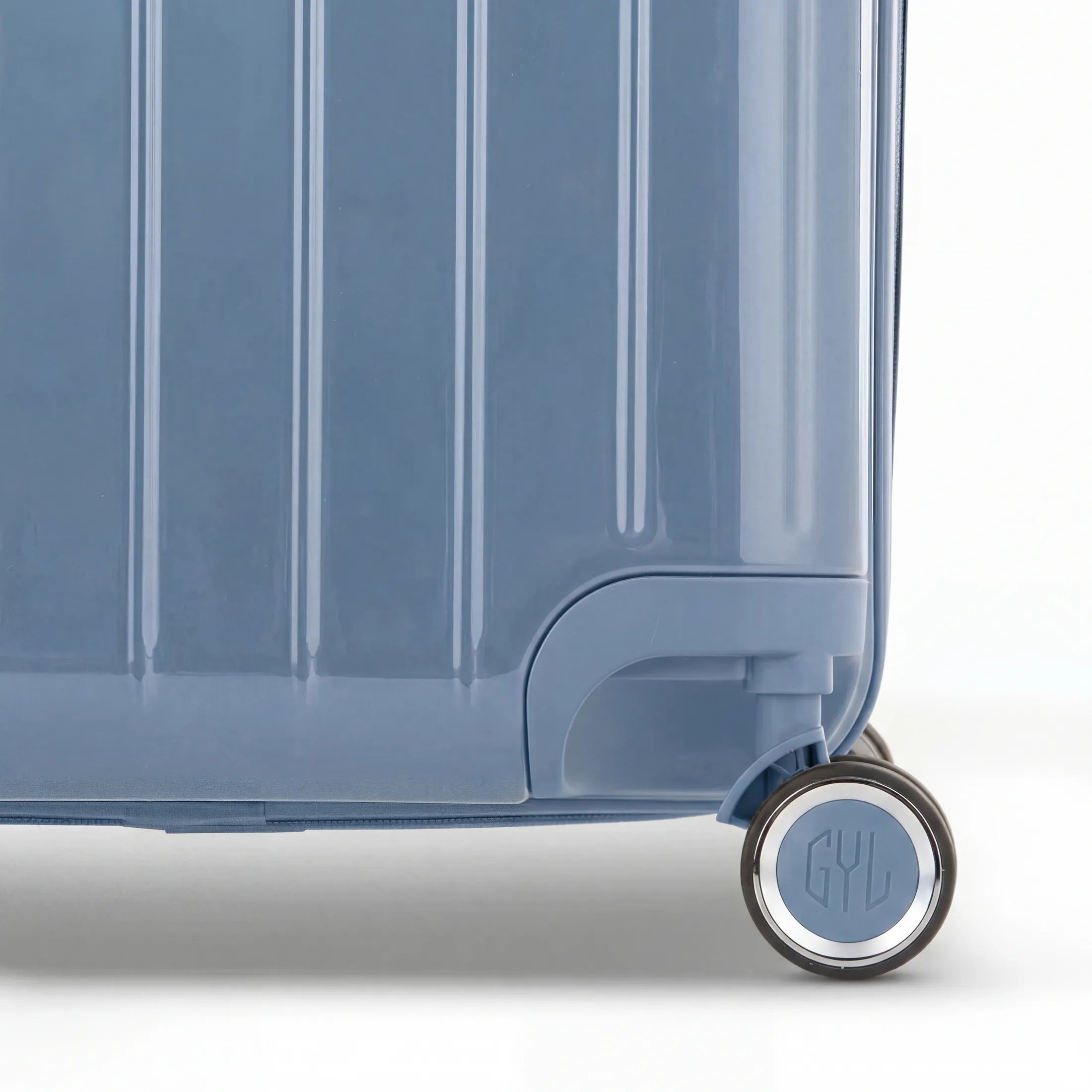 Détail de la roue et du logo GYL sur le bas de la valise trunk bleu gris en polycarbonate brillant.