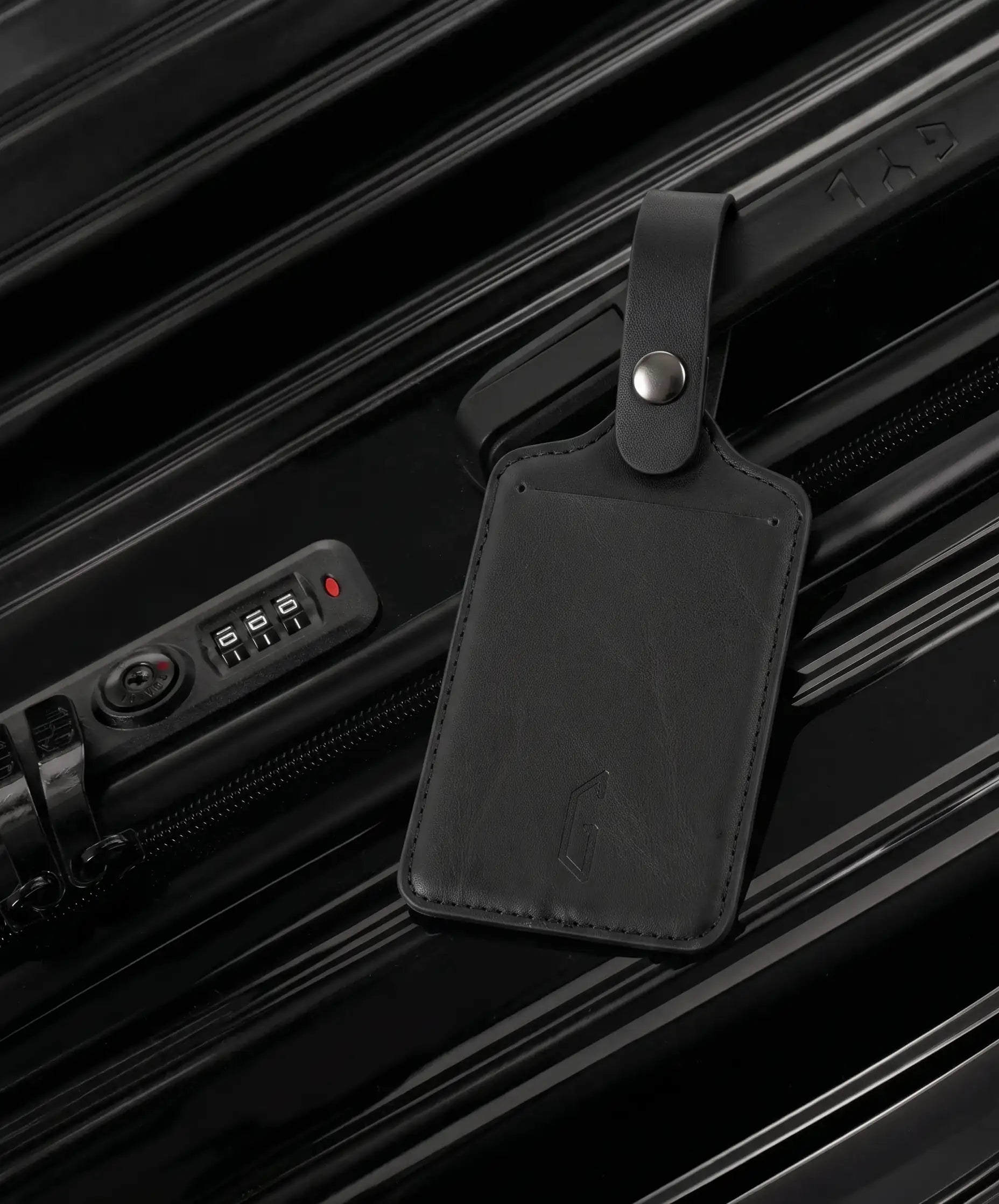 Etiquette de bagage GYL en cuir coloris noir fixee par sa bride a pression sur la poignee d'une valise GYL assortie