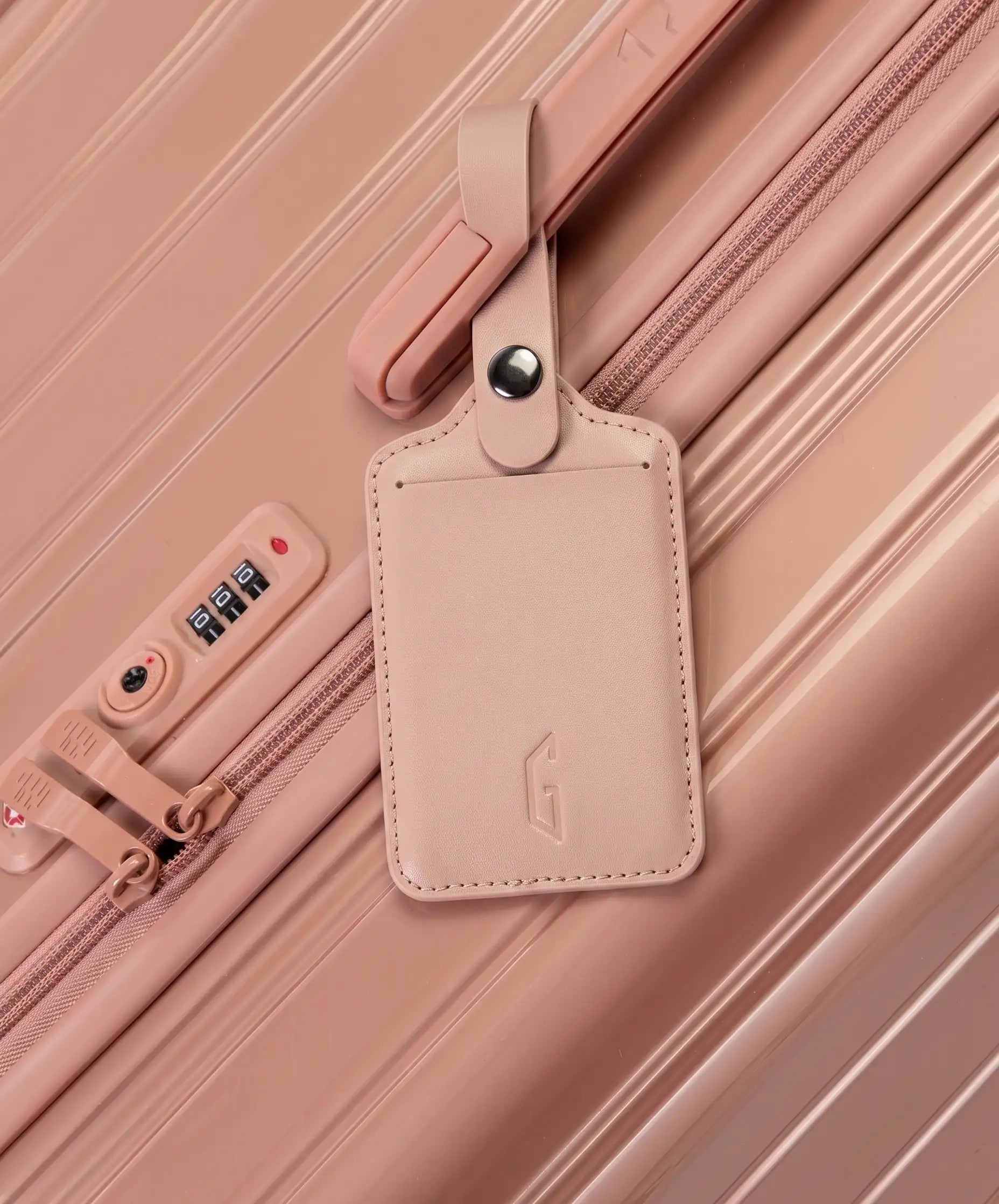 Etiquette de bagage GYL en cuir coloris rose gold fixee par sa bride a pression sur la poignee d'une valise GYL assortie