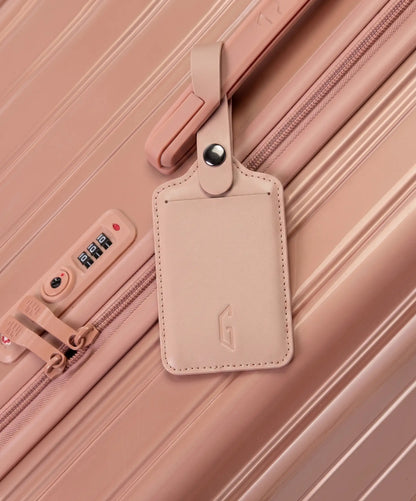 Etiquette de bagage GYL en cuir coloris rose gold fixee par sa bride a pression sur la poignee d'une valise GYL assortie