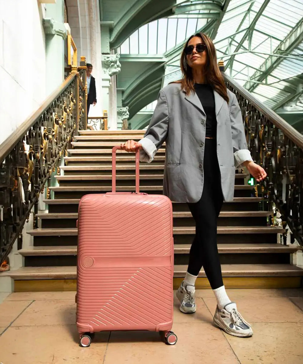 Femme stylée descendant un escalier dans une gare, tirant une grande valise rigide GYL rose poudré – bagage grand format au design élégant et fonctionnel.