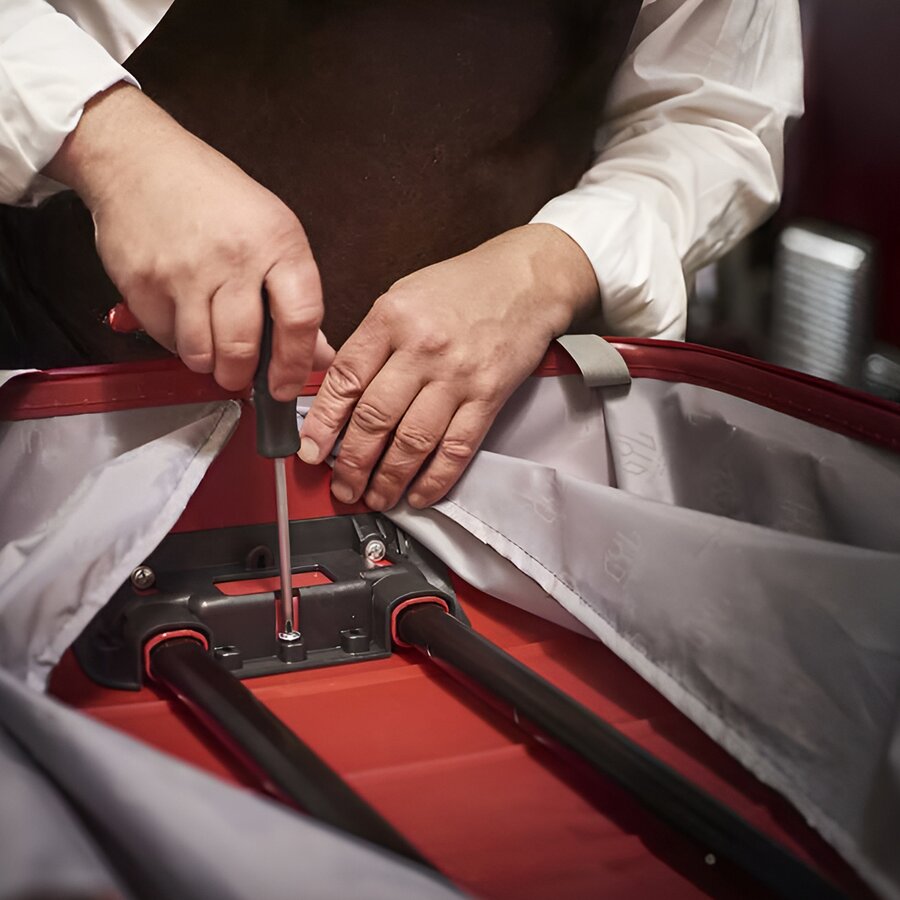 Artisan GYL réparant la poignée télescopique d'une valise rouge en atelier