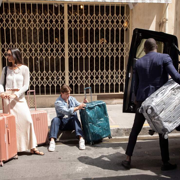 Voyageurs avec valises GYL rose, turquoise et argent dans une rue parisienne