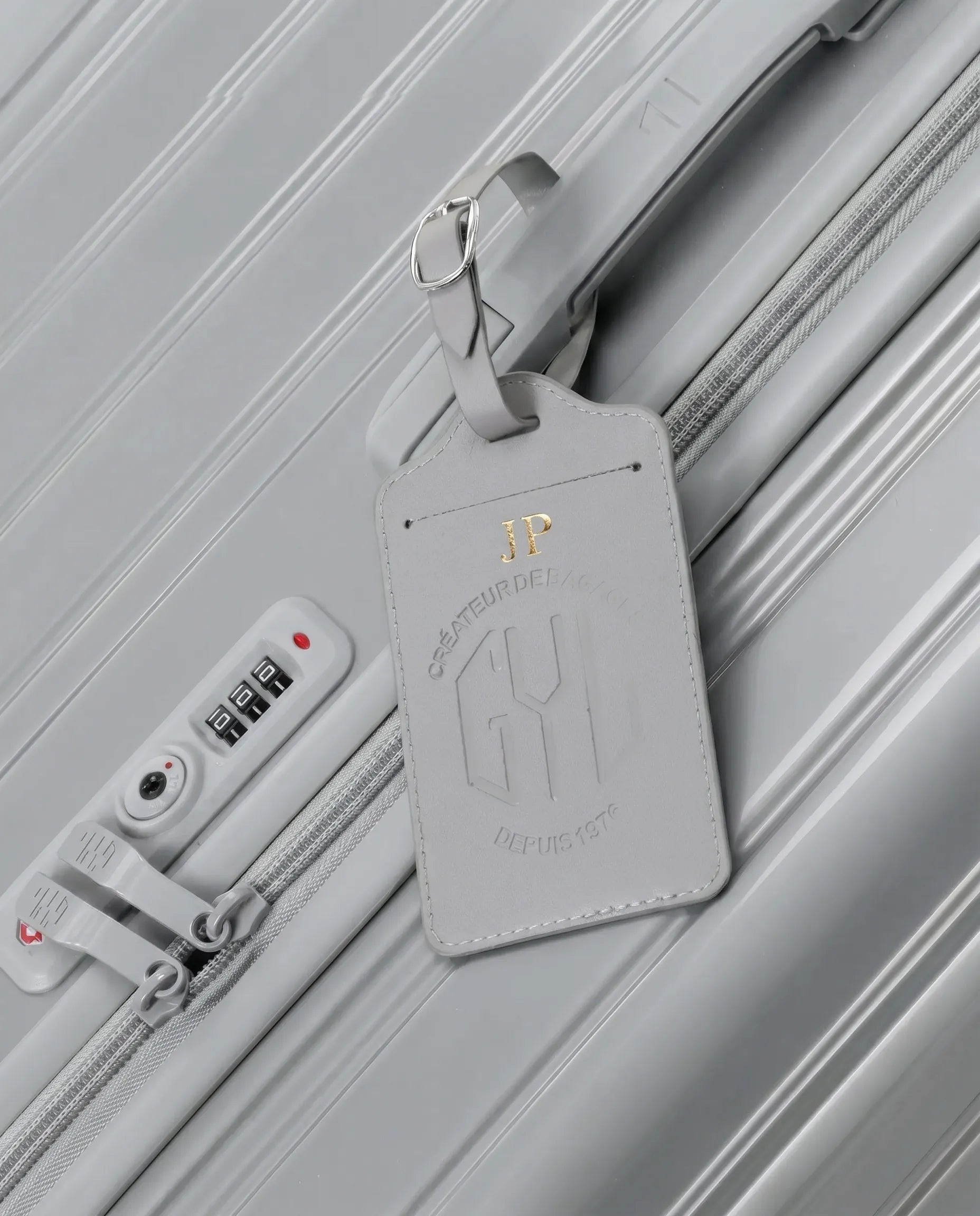 Etiquette a bagages GYL personnalisee initiales JP en feuille d'or, accrochee a une valise argent