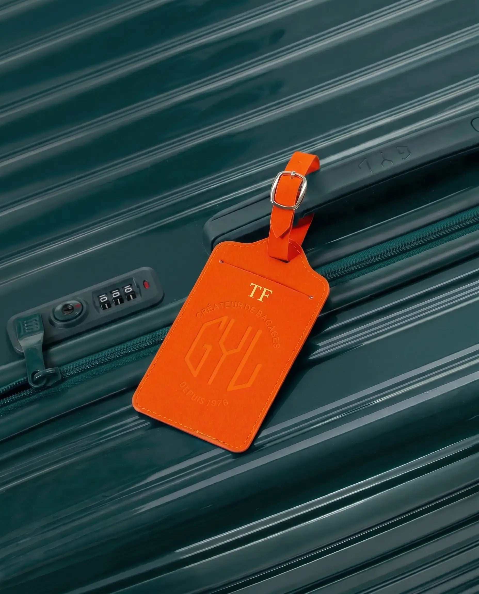 Etiquette a bagages GYL personnalisee initiales TF en feuille d'or, accrochee a une valise orange