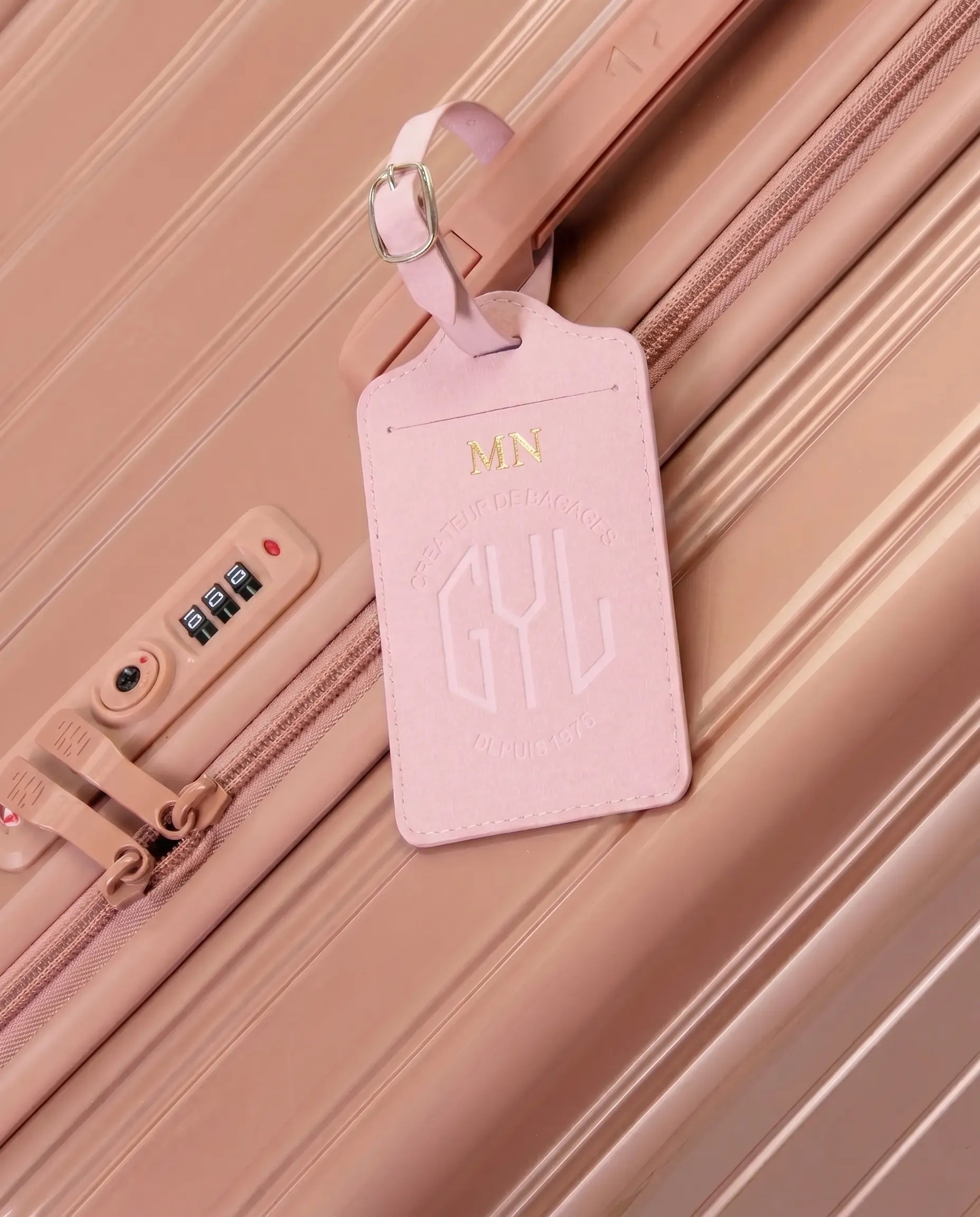 Etiquette a bagages GYL personnalisee initiales MN en feuille d'or, accrochee a une valise rose