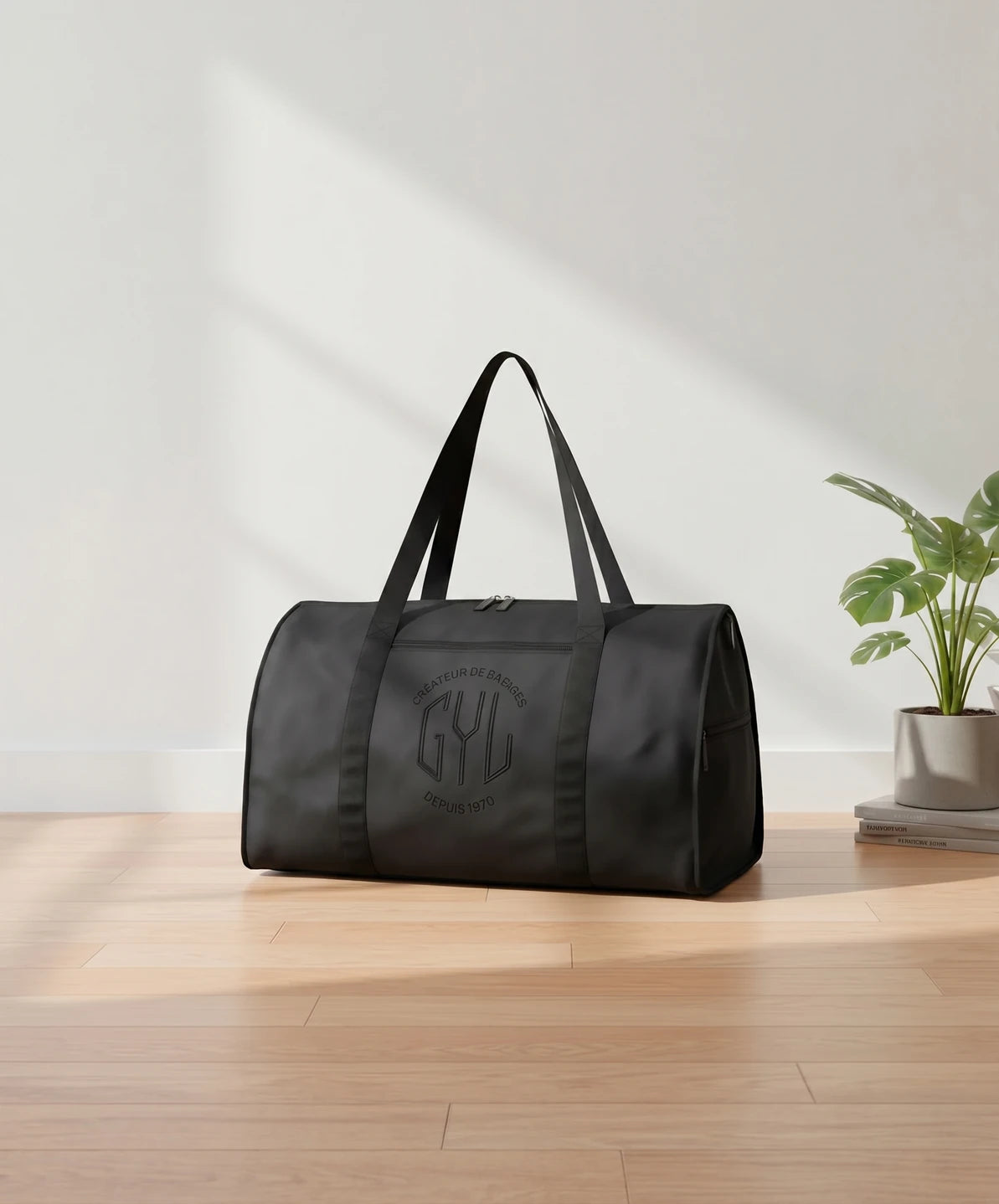 Sac de voyage pliant GYL coloris noir pose sur parquet bois clair avec plante monstera et livres