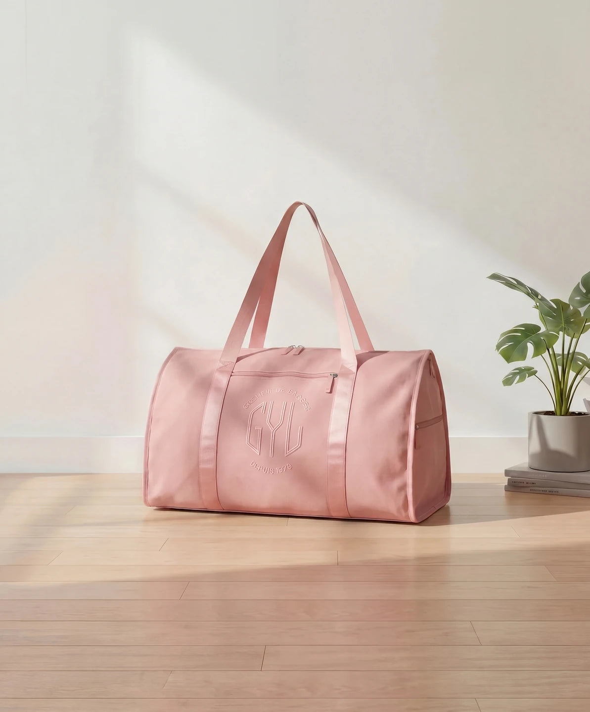 Sac de voyage pliant GYL coloris rose gold pose sur parquet bois clair avec plante monstera et livres